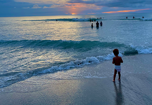 Bebê na praia com várias pessoas no mar